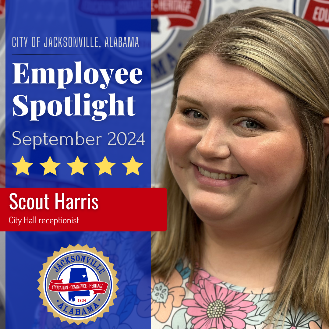 Picture of Jacksonville employee Scout Harris smiling, standing in front of the city seal. Text in a sidebar reads "City of Jacksonville Alabama, Employee Spotlight, September 2024, Scout Harris, City Hall receptionist," with another city seal lined in gold below it, and five gold stars above Harris' name.